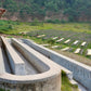 Concrete water trough in a rural setting with rows of raised beds in the background.