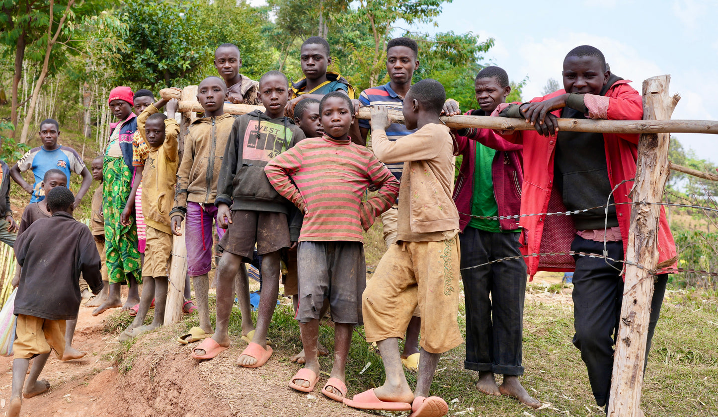 Group of children standing behind a wooden fence in a rural setting.