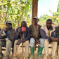 Four men sitting under a wooden shelter with trees in the background